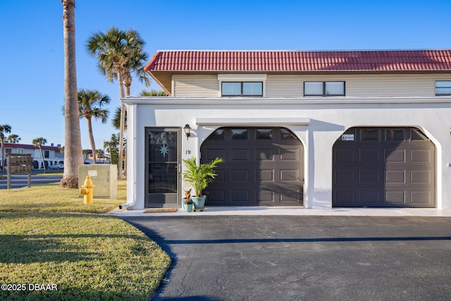 view of front facade featuring a garage, a front lawn, a tile roof, and stucco siding