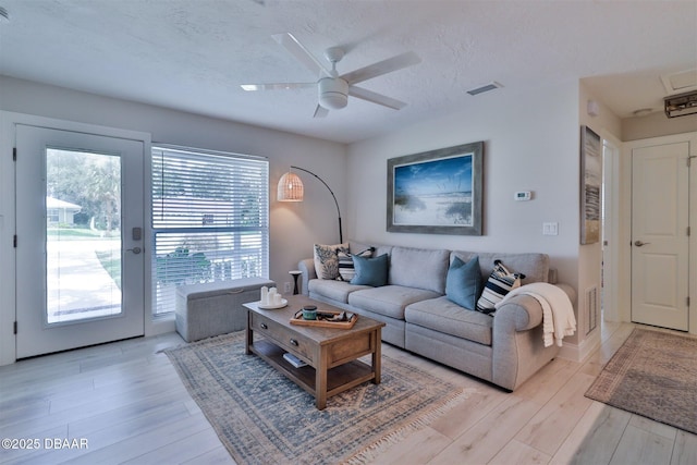 living room featuring ceiling fan, a textured ceiling, light wood-type flooring, and a healthy amount of sunlight