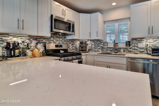 kitchen with appliances with stainless steel finishes, light stone countertops, sink, white cabinetry, and tasteful backsplash