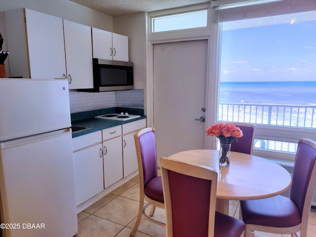 kitchen featuring a water view, white cabinetry, tasteful backsplash, light tile patterned floors, and white appliances