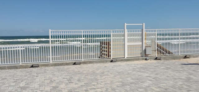 view of gate featuring a water view and a beach view