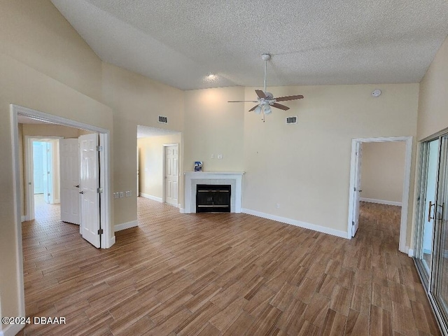 unfurnished living room with a textured ceiling, high vaulted ceiling, light hardwood / wood-style floors, and ceiling fan