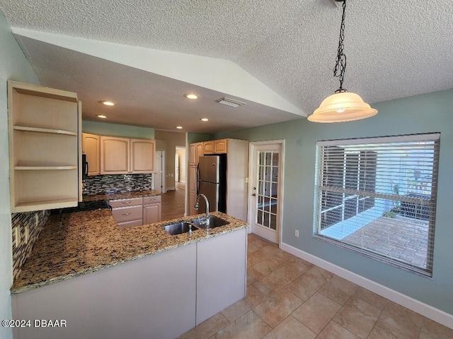 kitchen with lofted ceiling, kitchen peninsula, stainless steel refrigerator, pendant lighting, and light brown cabinetry