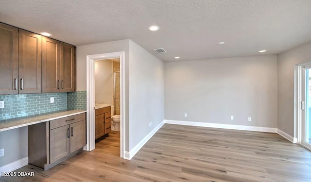 kitchen with backsplash, a textured ceiling, and light hardwood / wood-style flooring