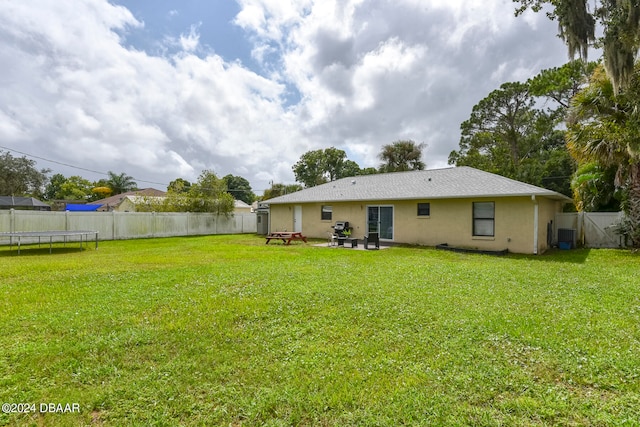 rear view of property featuring a lawn, central AC, a patio, and a trampoline