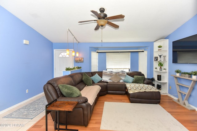 living room featuring built in shelves, light wood-type flooring, ceiling fan, and vaulted ceiling