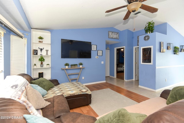 living room featuring built in shelves, vaulted ceiling, ceiling fan, and light hardwood / wood-style flooring