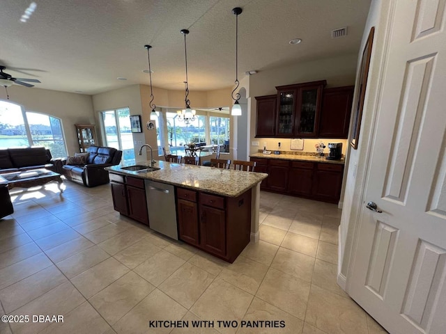 kitchen with stainless steel dishwasher, decorative light fixtures, dark brown cabinetry, light stone counters, and a center island with sink