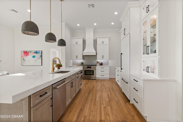 kitchen featuring premium range hood, sink, appliances with stainless steel finishes, decorative light fixtures, and white cabinetry