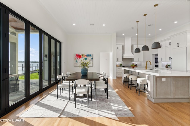 dining room with sink, light wood-type flooring, a water view, wood ceiling, and ornamental molding