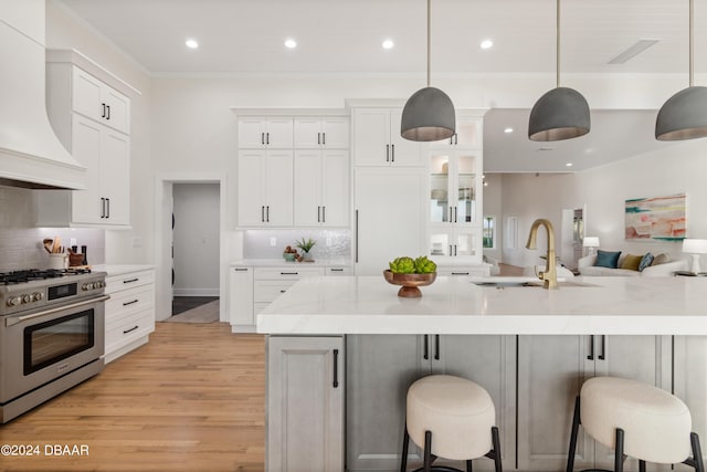 kitchen featuring sink, high end stainless steel range oven, decorative light fixtures, a breakfast bar, and custom range hood