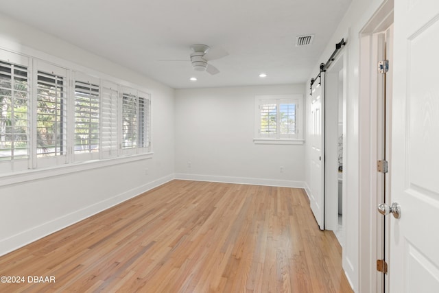 unfurnished room featuring a barn door, a wealth of natural light, ceiling fan, and light wood-type flooring