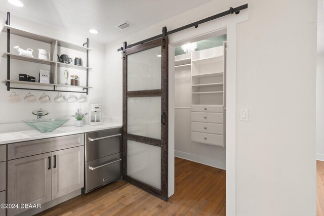 bar featuring a barn door, light stone counters, and hardwood / wood-style flooring