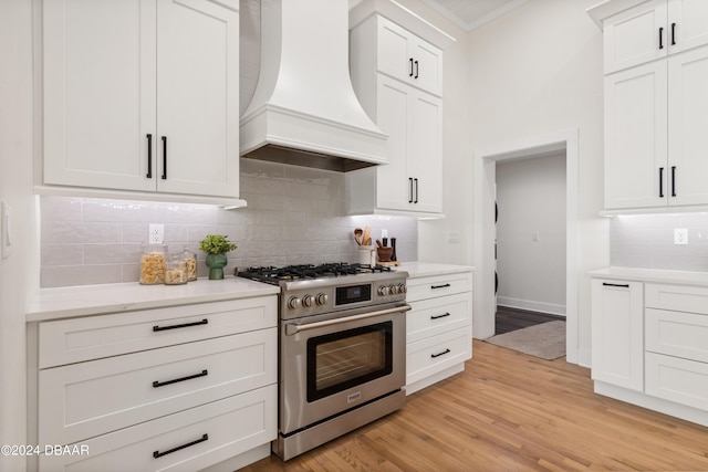 kitchen with tasteful backsplash, white cabinetry, stainless steel range, and custom exhaust hood