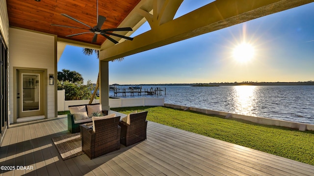 deck at dusk with ceiling fan, a yard, and a water view