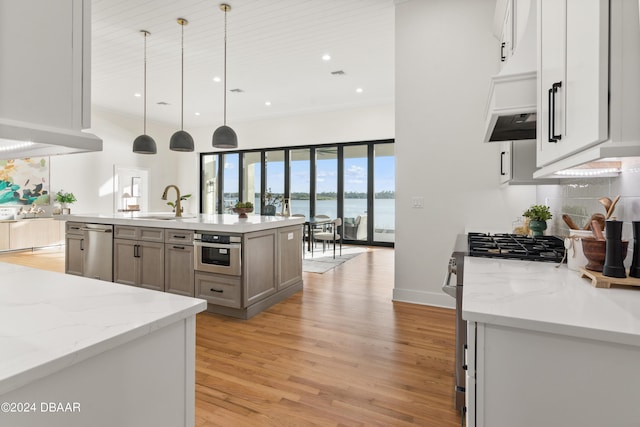 kitchen with light stone counters, stainless steel appliances, decorative light fixtures, a water view, and an island with sink