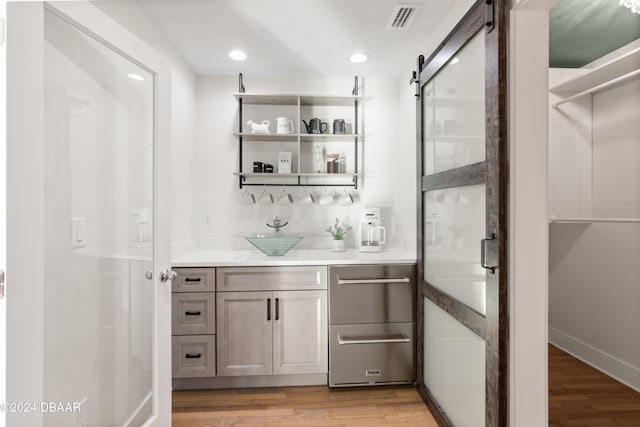 bar with light wood-type flooring, a barn door, gray cabinets, and sink