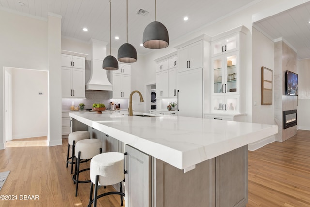 kitchen featuring a large island with sink, white cabinetry, wooden ceiling, and custom exhaust hood