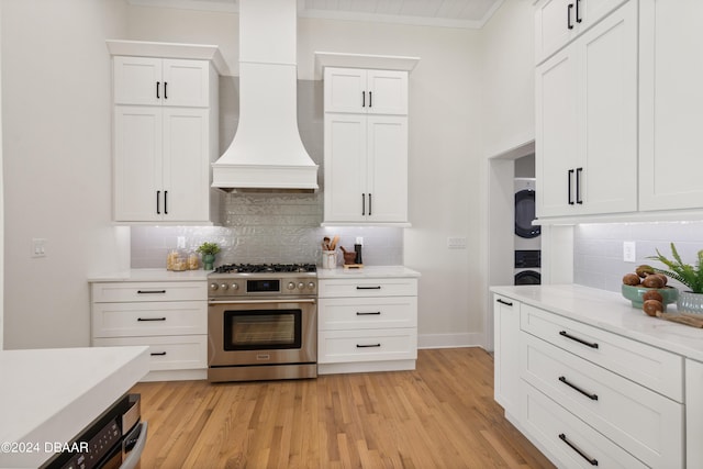 kitchen featuring high end stove, backsplash, white cabinets, and custom range hood