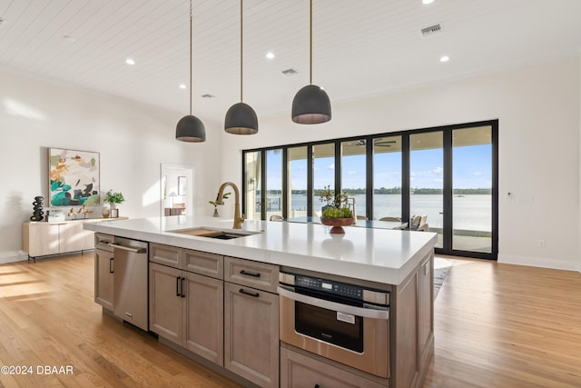 kitchen with sink, stainless steel appliances, decorative light fixtures, a center island with sink, and a water view