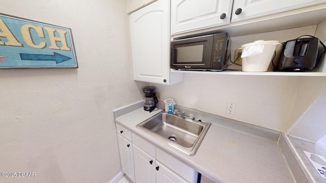 kitchen with white cabinets, light countertops, black microwave, and a sink