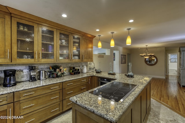 kitchen featuring kitchen peninsula, black electric stovetop, light stone countertops, and pendant lighting