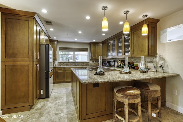 kitchen featuring stainless steel refrigerator, light stone countertops, hanging light fixtures, kitchen peninsula, and decorative backsplash