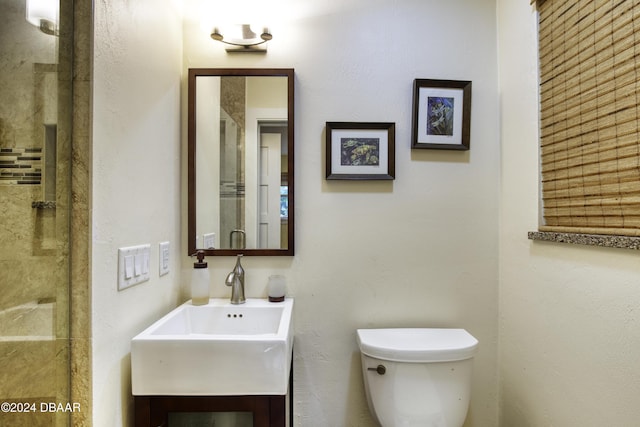 bathroom featuring toilet, a shower with shower door, and sink