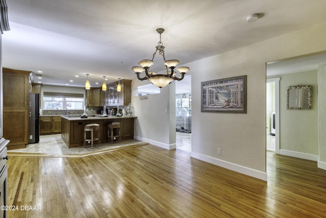 kitchen with an inviting chandelier, a kitchen breakfast bar, backsplash, pendant lighting, and light wood-type flooring