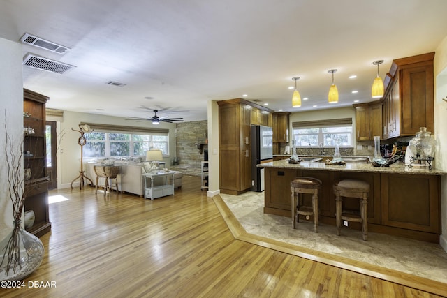 kitchen featuring hanging light fixtures, decorative backsplash, light hardwood / wood-style floors, light stone counters, and kitchen peninsula