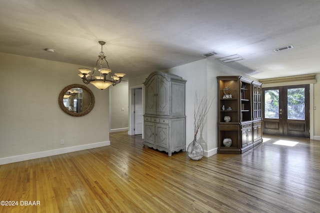 unfurnished living room with french doors, an inviting chandelier, and hardwood / wood-style floors