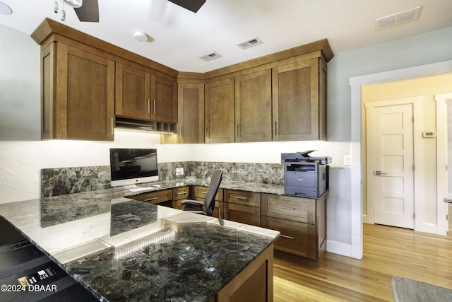 kitchen with ceiling fan, light hardwood / wood-style floors, kitchen peninsula, and dark stone counters