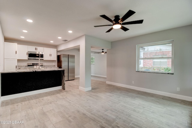 kitchen with white cabinetry, light wood-type flooring, light stone countertops, and appliances with stainless steel finishes