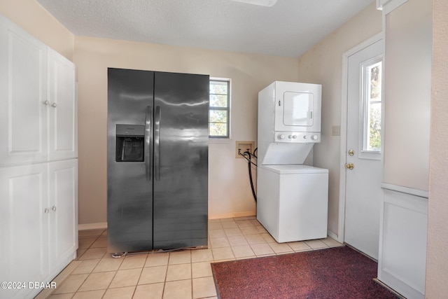 clothes washing area featuring a textured ceiling, light tile patterned floors, and stacked washer / drying machine