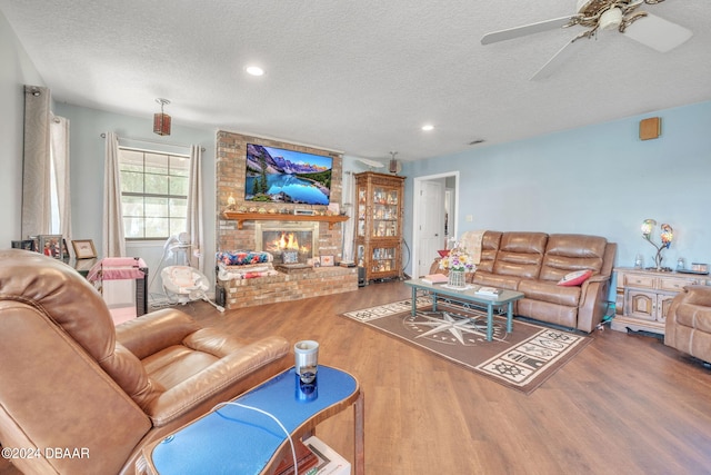 living room with hardwood / wood-style floors, a fireplace, a textured ceiling, and ceiling fan