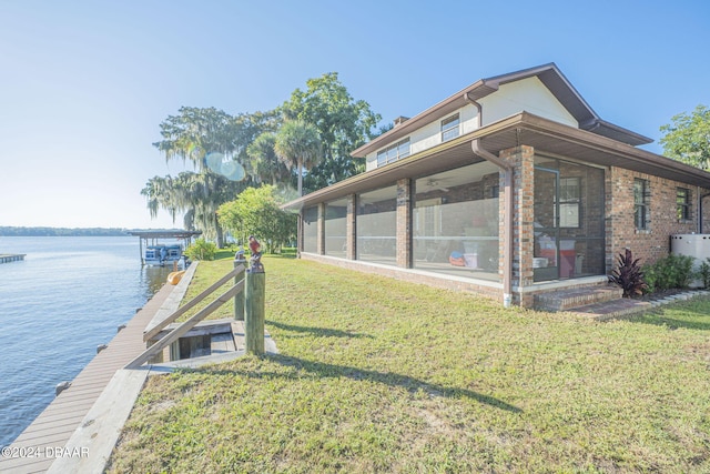 view of side of home featuring a sunroom, a water view, a lawn, and a boat dock