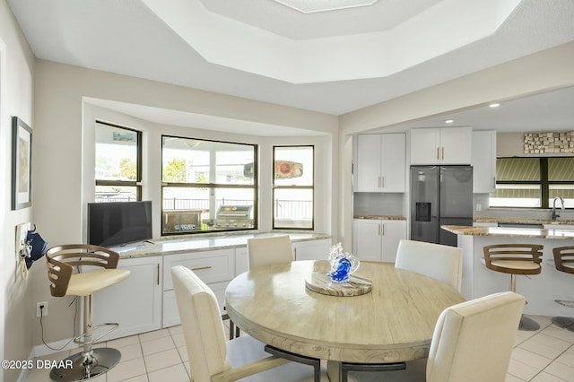 dining space with light tile patterned floors, a raised ceiling, and sink