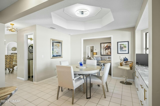 dining space featuring a chandelier, light tile patterned floors, and a raised ceiling