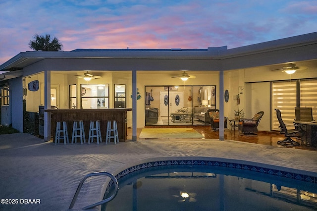 back house at dusk with a bar, ceiling fan, and a patio area