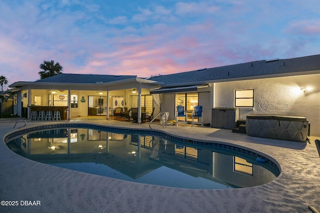 pool at dusk with a patio area and a bar