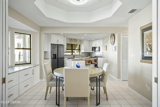 dining area featuring light tile patterned flooring, sink, and a tray ceiling