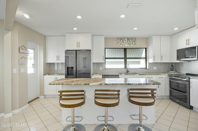 kitchen featuring white cabinets, light stone countertops, a kitchen island, and appliances with stainless steel finishes