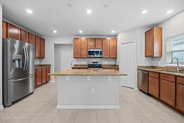 kitchen with stainless steel appliances, a kitchen island, sink, and light stone counters