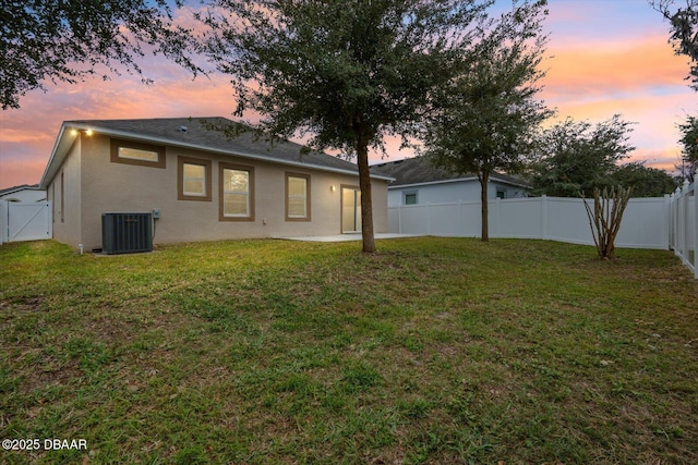 back house at dusk featuring a lawn and central air condition unit