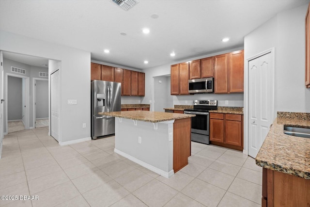 kitchen featuring light tile patterned floors, a kitchen island, stainless steel appliances, light stone countertops, and a kitchen bar