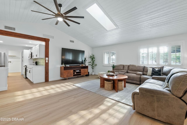 living room with ceiling fan, high vaulted ceiling, light wood-type flooring, and a skylight