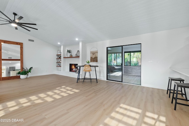 living room with ceiling fan, a fireplace, light hardwood / wood-style floors, and vaulted ceiling