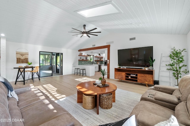 living room with ceiling fan, light hardwood / wood-style floors, and vaulted ceiling with skylight