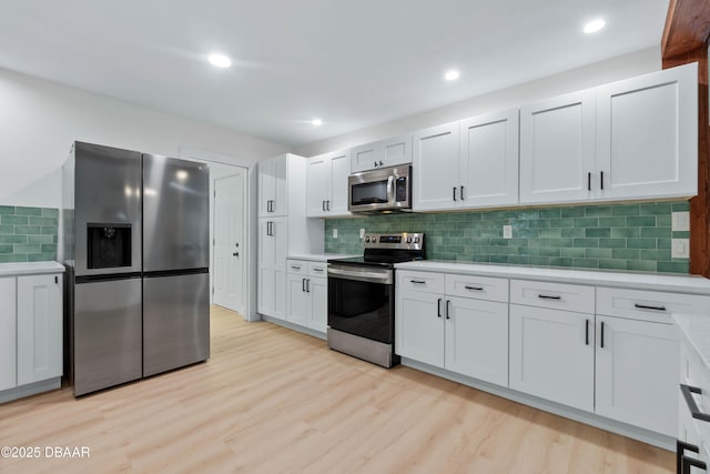 kitchen with white cabinetry, backsplash, light hardwood / wood-style floors, and appliances with stainless steel finishes