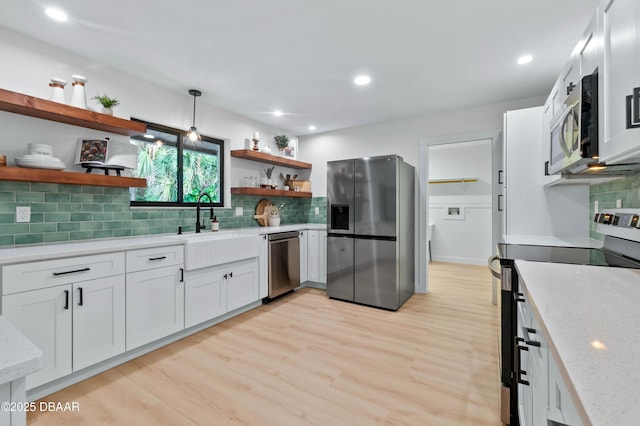 kitchen featuring appliances with stainless steel finishes, white cabinetry, sink, hanging light fixtures, and light stone counters